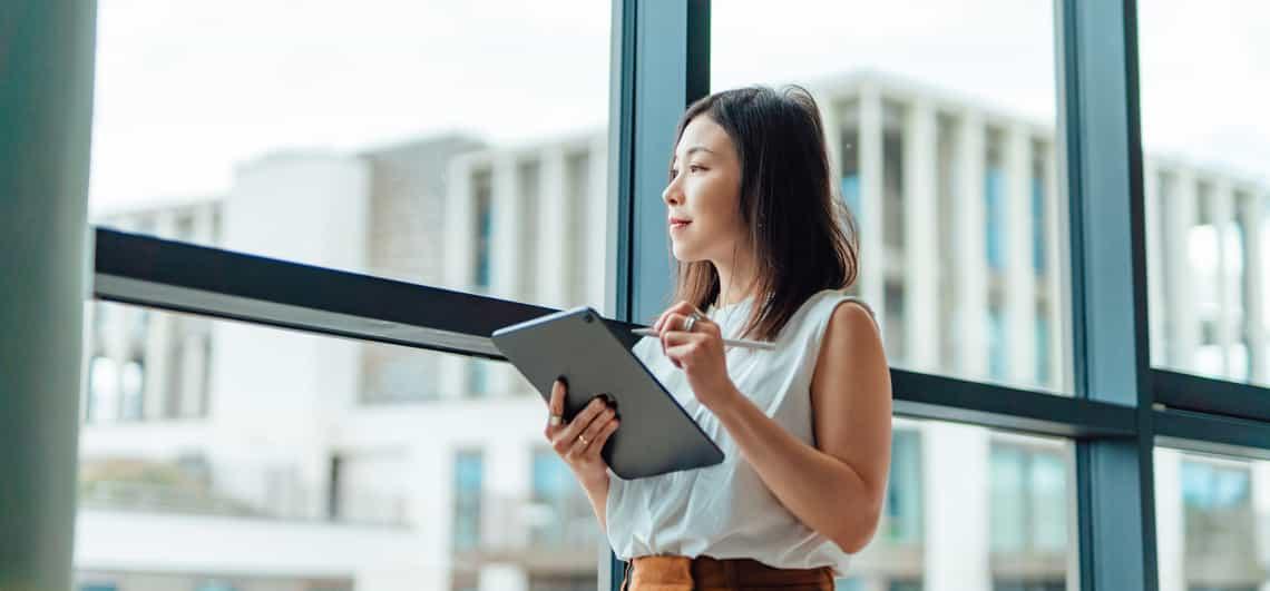 young account manager using an account planning tool on a tablet looking out the window smiling because the tool is helping her grow her revenue.