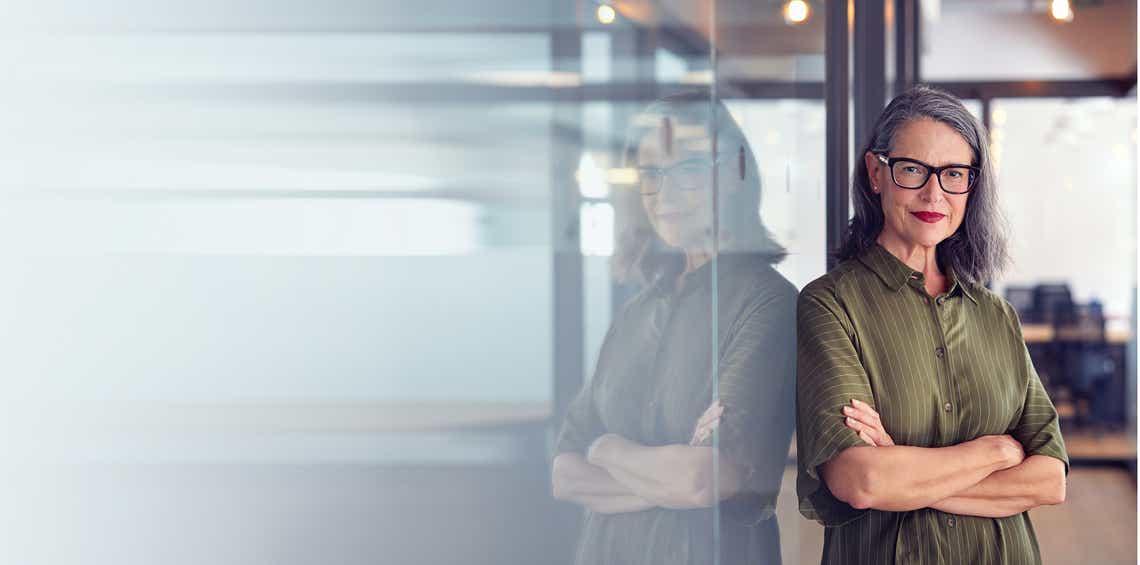 senior sales leader leaning against a glass wall looking at the camera happy with the changes she is successfully leading her sales organization through as a result of the skills she built in the leaders leading change training program